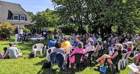 Menschen sitzen auf Stühlen im Garten bei einem Konzert mit Musikern und Sprechern