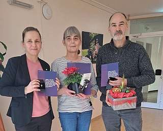 Drei Personen halten Geschenke und Pflanzen in einem Raum.